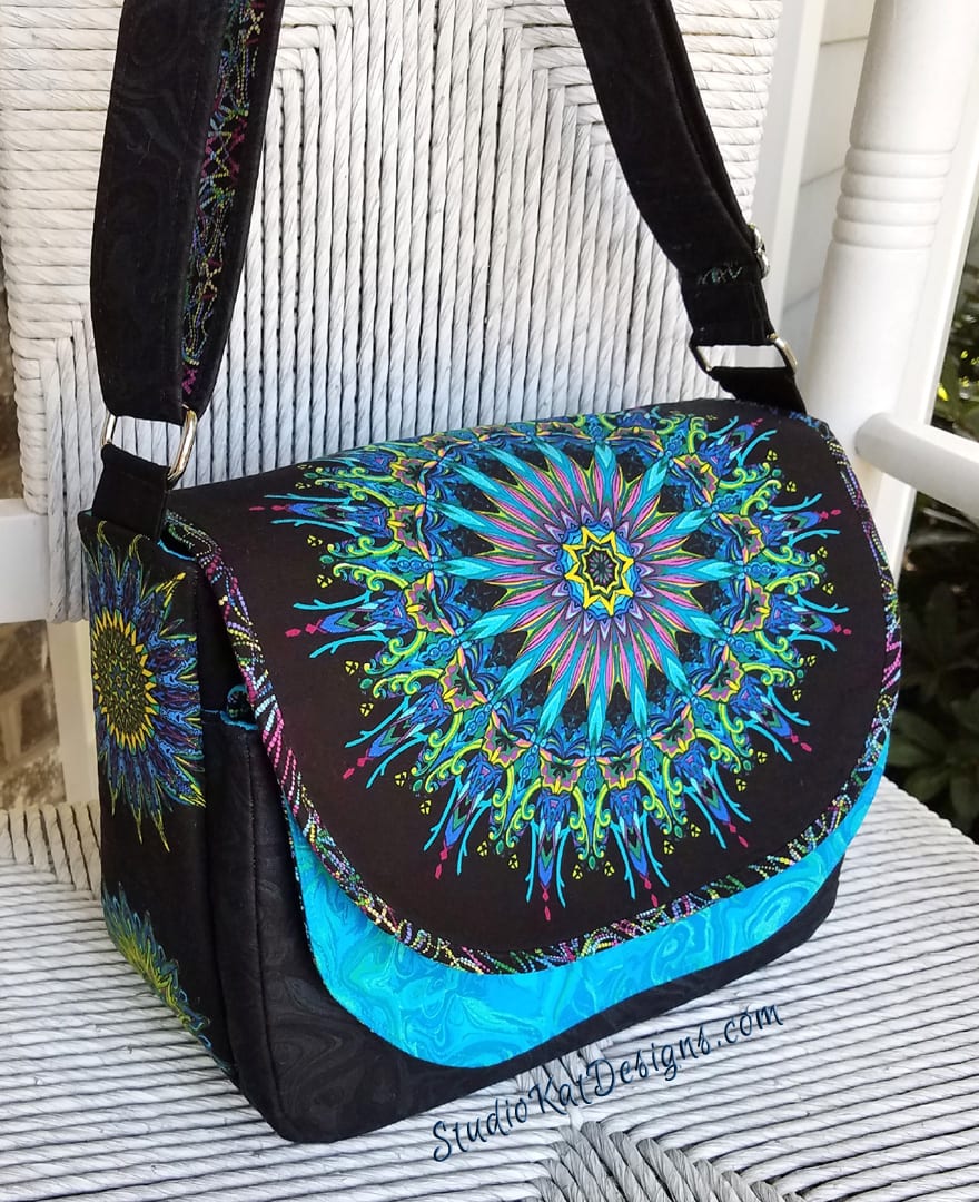 Colorful mandala-patterned shoulder bag with black strap.