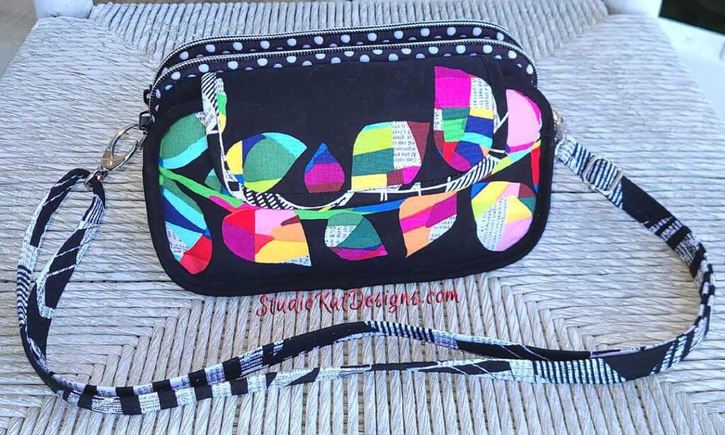 A black cross body bag with a colorful design on it.