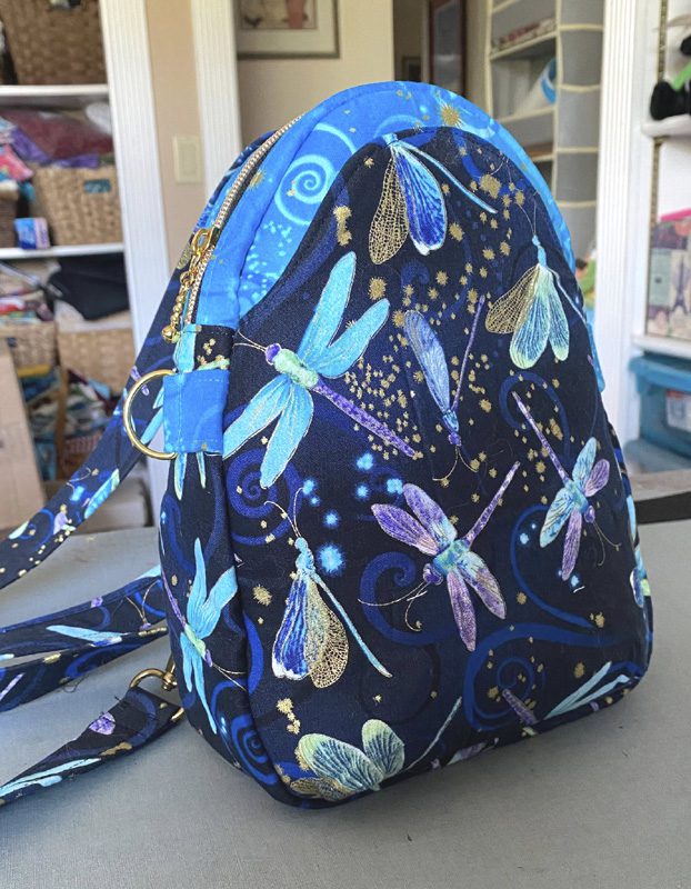 Backpack with colorful dragonfly and butterfly pattern on dark background.