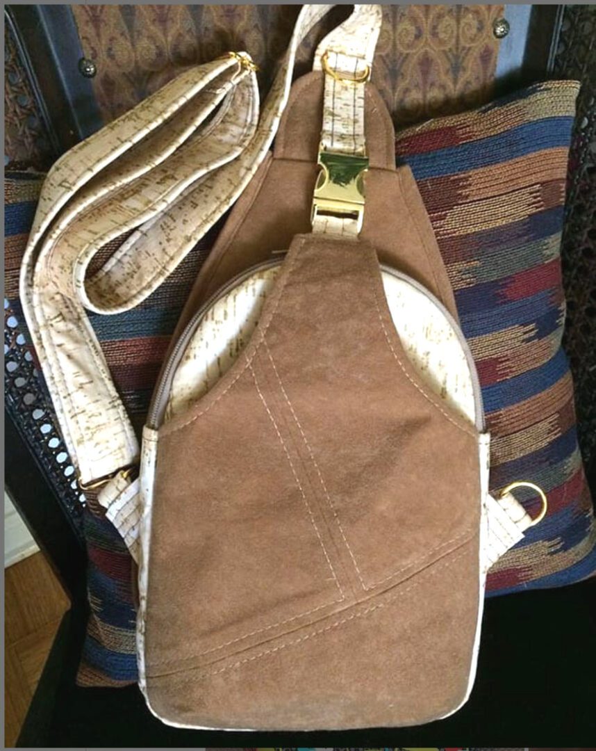 Brown suede sling backpack with gold strap and buckle.