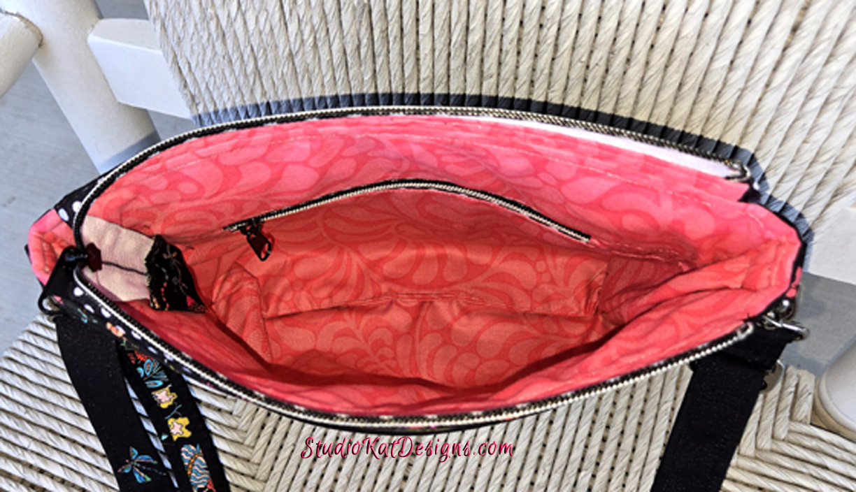 Open handbag showing pink interior lining and zippered pocket.