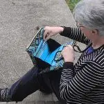 A woman sitting on a sidewalk holding a purse.