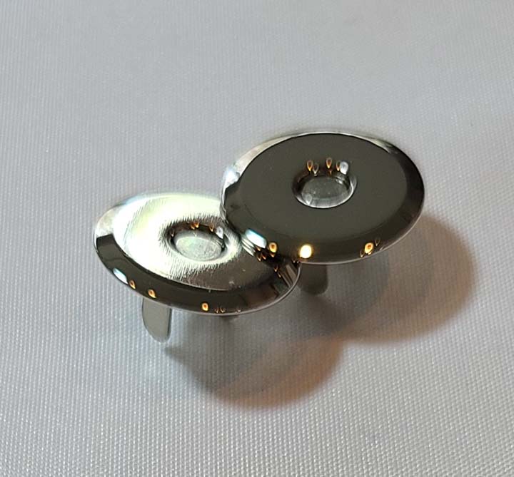 A pair of silver metal buttons on a white surface.