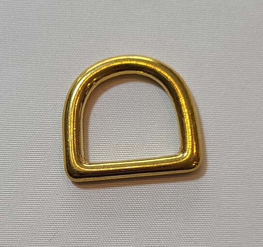 A gold plated d ring on a white surface.