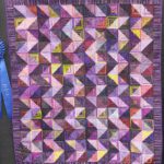 A purple quilt with a ribbon on it.