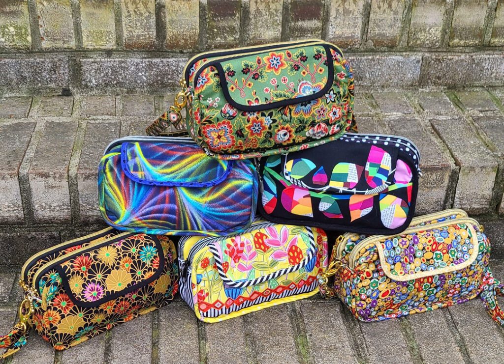 A group of colorful handbags sitting on a brick walkway.