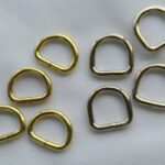 A set of brass d-rings on a white surface.