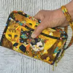 A person holding a yellow purse with cats on it.
