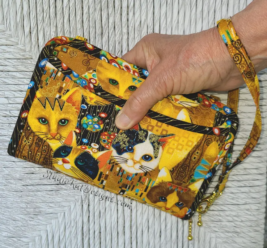 A person holding a yellow purse with cats on it.