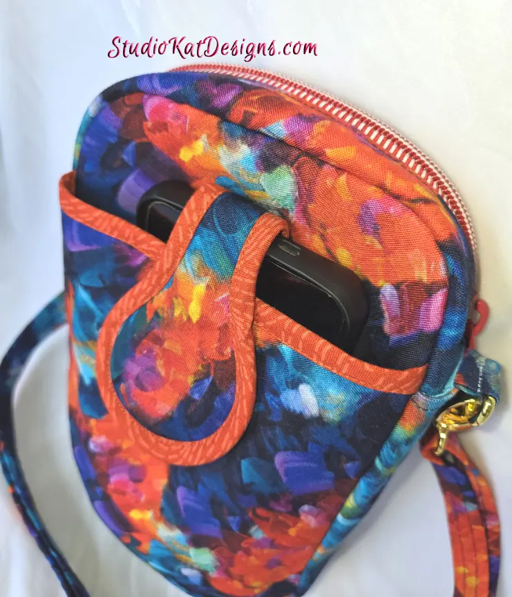 Colorful abstract patterned pouch with zipper and strap.
