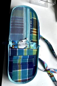 A small white hamster peeks out from a colorful fabric pouch.