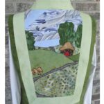 Quilted fabric art depicting a scenic countryside landscape on a green vest. Quilted fabric art depicting a scenic countryside landscape on a green vest.