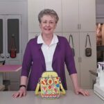 Woman smiling behind colorful handbag in a kitchen.