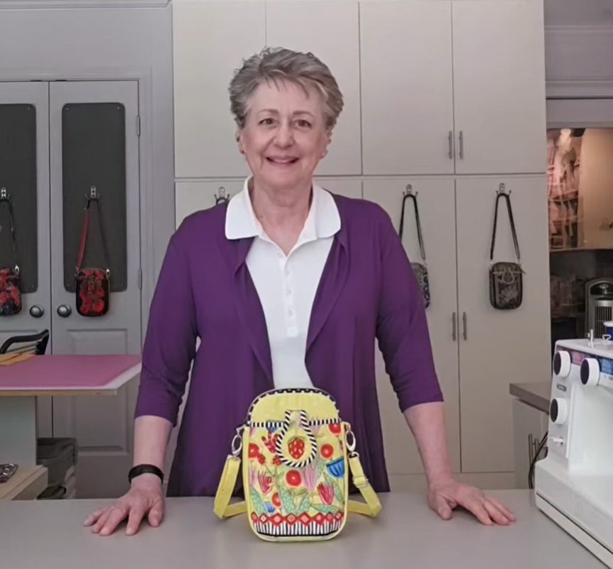 Woman smiling behind colorful handbag in a kitchen.