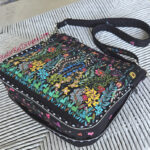 Colorful floral embroidered shoulder bag with black strap and studded edges.