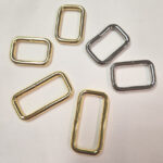Various small metal rectangular rings in gold and silver colors on a white surface.